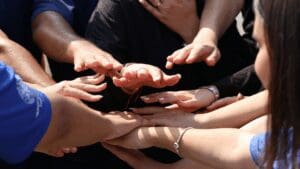 “Group of diverse hands stacked together, symbolizing teamwork, trust, and accountability in Neuroscience-Based Executive Coaching.”