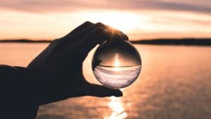 Hand holding a glass sphere reflecting a sunset, symbolizing the illusion and allure behind why we want what we can't have.