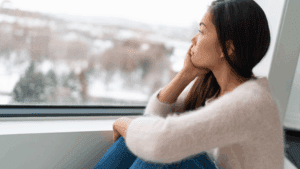 Woman sitting by a window looking outside thoughtfully, reflecting on desire and why we want what we can't have.