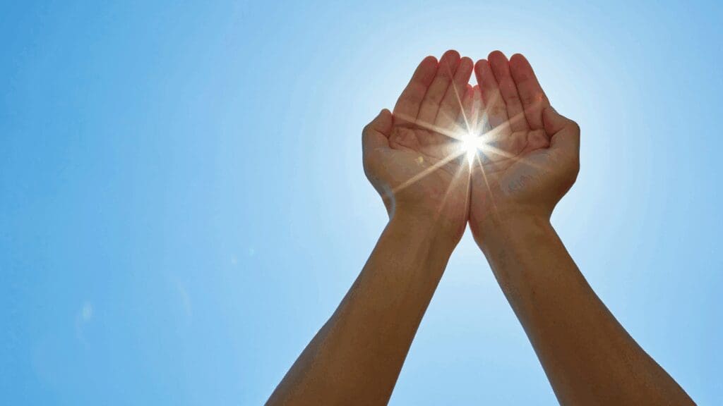 Hands cupped together holding bright sunlight against a clear blue sky, symbolizing the positive transformation and motivation achieved through dopamine coaching.