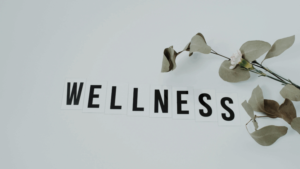Wellness text spelled out on white tiles with fresh eucalyptus branch, representing holistic dopamine mental health and well-being achieved through neuroscience-based lifestyle optimization.