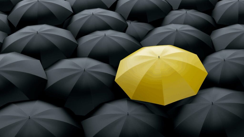 Yellow umbrella standing out among black umbrellas symbolizing differentiation in life coaching vs neuroscience coaching