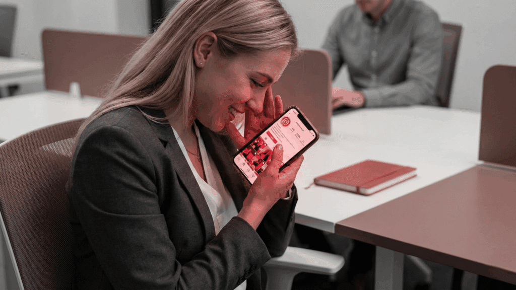 A smiling woman in an office looks at her phone with affection, capturing the emotional anticipation reflected in the neuroscience of love.
