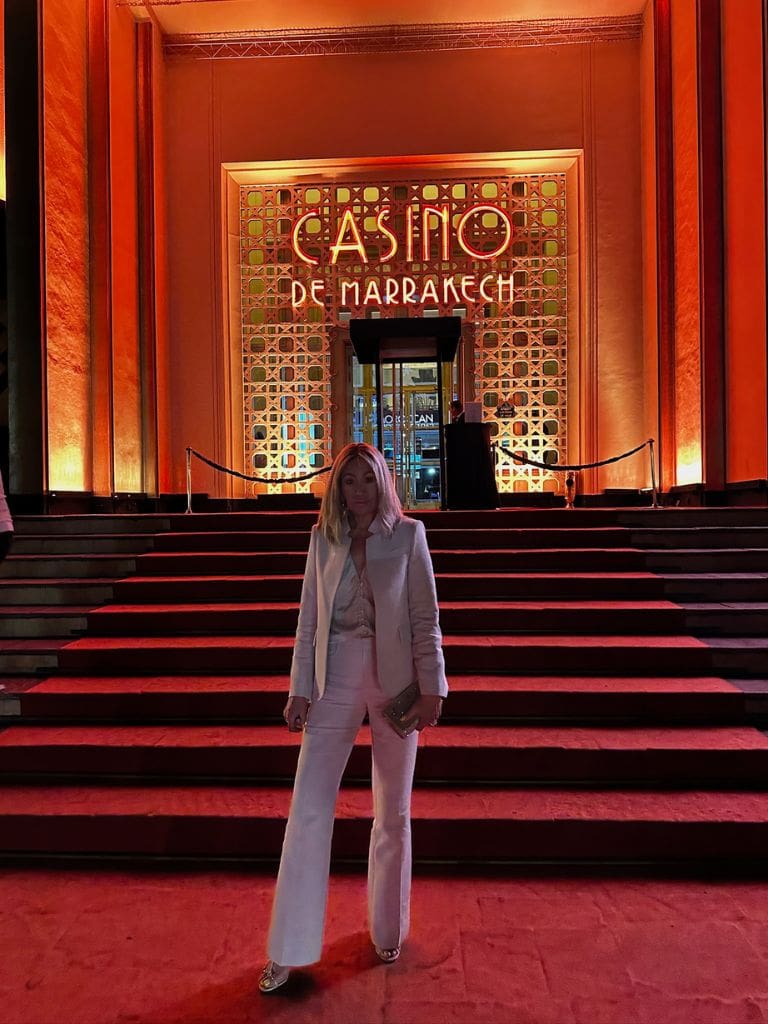 Dr. Sydney Ceruto in an elegant white suit standing on the grand red-carpeted steps of Casino De Marrakech at night